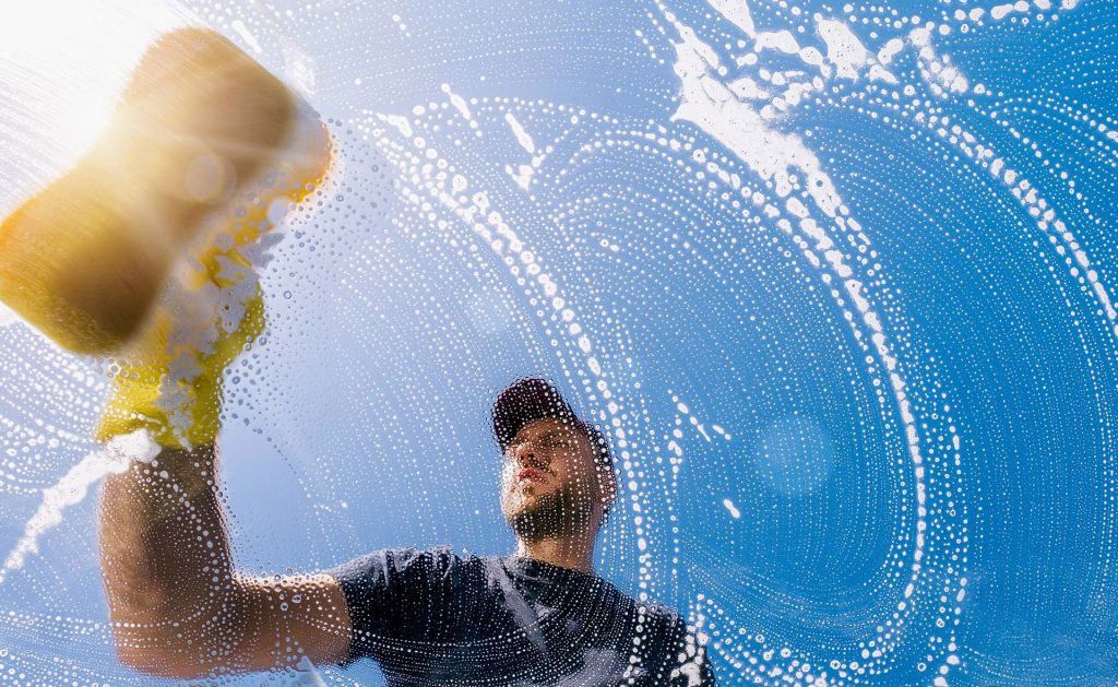 A man uses a squeegee to clean a window, removing dirt and streaks.