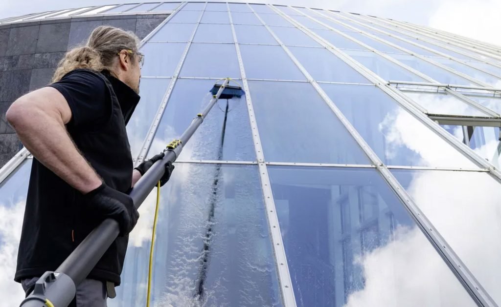 A man uses a hose to clean building glass, maintaining its exterior