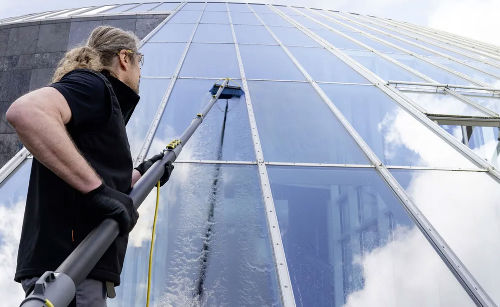 A man uses a hose to clean building glass, maintaining its exterior