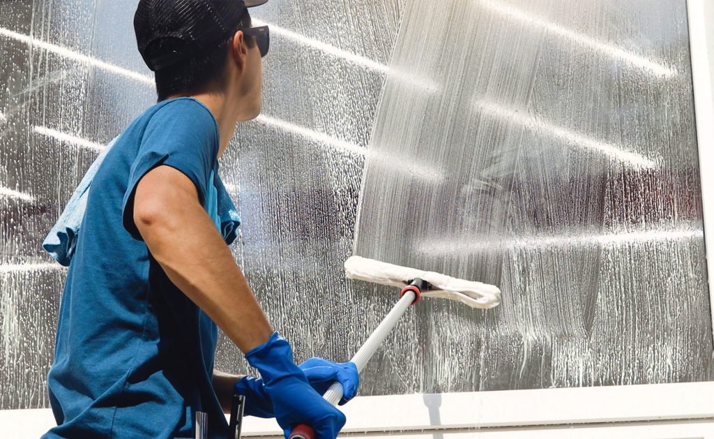A man in a blue shirt and gloves cleans a window, enhancing visibility