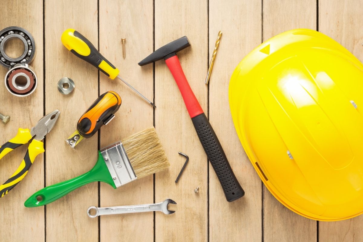 A variety of construction tools, including a hammer, screwdriver, and tape measure, arranged on a wooden floor.