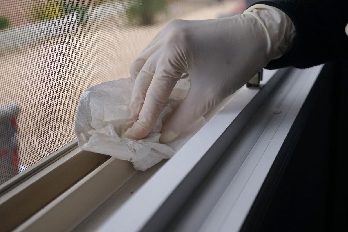  A person wearing gloves diligently cleans a window, showcasing a homemade window cleaning method.