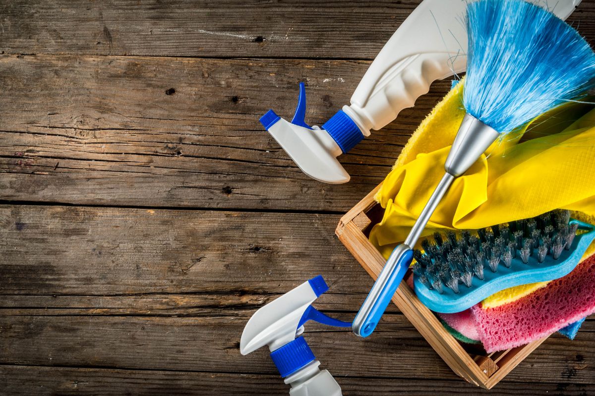 A collection of window cleaning products arranged in a wooden crate on a textured wooden surface.
