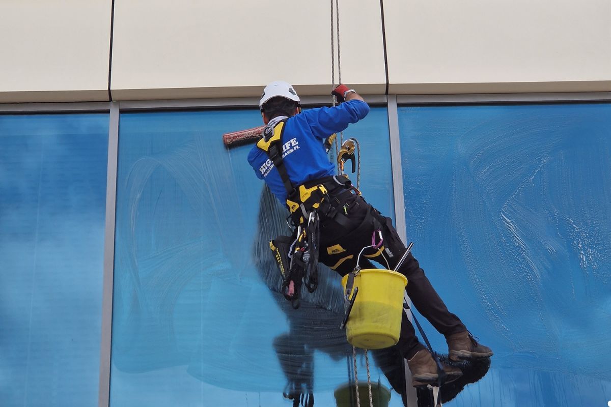 A man wearing a blue shirt and vest cleans a window with a cloth, focused on his task. 