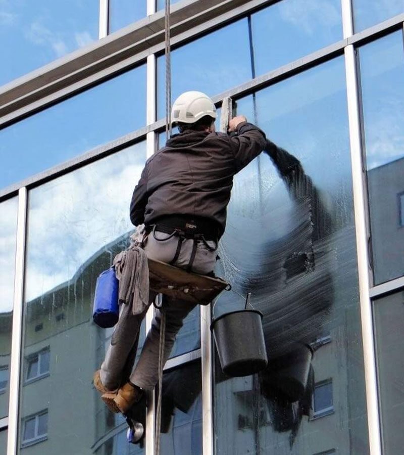 A man in a hard hat cleans windows, ensuring clarity and safety
